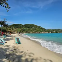 Solig strand på Koh Phangan, Thailand. Turkost vatten, gröna kullar och tomma solstolar väntar på besökare.