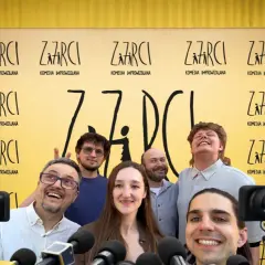 Uśmiechnięta ekipa "ZARCI KOMEDIA IMPROWIZOWANA" przed żółtym tłem z logo. Wrocławski teatr komedii gotowy na wywiady.