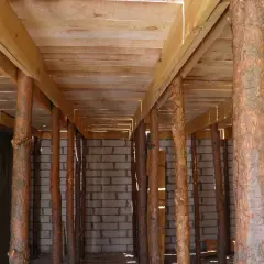 Szalowanie stropu z drewnianych belek i pni drzewnych, podtrzymujące konstrukcję nad betonowymi ścianami.
