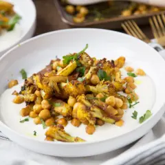Chou-fleur rôti aux épices, pois chiches et sauce crémeuse. Un délice de chou fleur barbecue, garni de persil frais.
