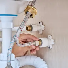Mano conectando una manguera a la llave de paso de agua general, parte de la fontanería bajo un lavabo.