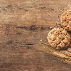 Chleb pełnoziarnisty z ziarnami i kłosy zbóż na drewnianym tle. Jaki chleb przy hashimoto? Wybieraj ten z dobrych składników.