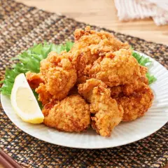 Chrupiące, złociste karaage na talerzu z sałatą i cytryną, obok szklanka złocistego napoju i pałeczki.