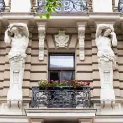 Dwie rzeźby atlantesów podtrzymują balkon z kwiatami. To przykład stylu secesja, co to za sztuka!