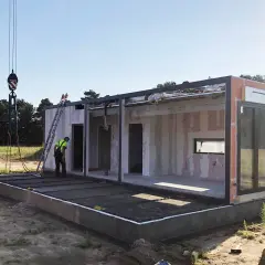 Budowa domu modułowego w toku. Dźwig podnosi element, pracownicy nadzorują montaż. To etap, gdy pozwolenie na budowę i prawo budowlane są kluczowe.