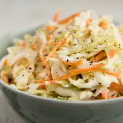 En skål med krämig, krispig coleslaw med strimlad vitkål och morötter, toppad med svartpeppar. Perfekt som tillbehör till grillat, detta är den godaste coleslaw!