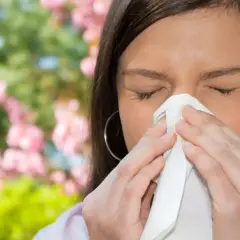 Mujer con alergia estornuda en un pañuelo, mostrando para que sirven los mocos: atrapar polen y alérgenos.