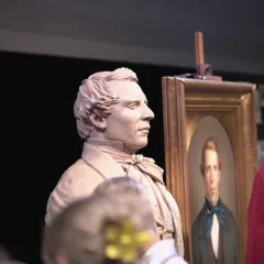 A clay bust of a man stands next to his portrait, perhaps a tribute to who is the most famous sculptor.