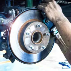 Mécanicien remplaçant la garniture de frein usure d'une Mercedes. Le disque de frein est visible, ainsi que les mains sales du technicien.