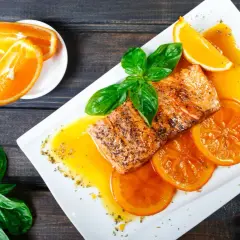 Delicioso salmón a la naranja, servido con rodajas de naranja y hojas de albahaca fresca.