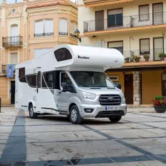 Biały kamper Benimar Sport 363 zaparkowany na brukowanym placu przed kamienicami.