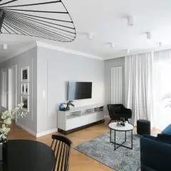 Nowoczesna aranżacja mieszkania w bloku 60 m. Salon z granatową kanapą, czarnym fotelem i stolikami. W tle kuchnia i jadalnia.