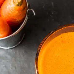 Frische Karotten in einem Eimer neben einem Glas leuchtend orangem Karottensaft. Die Wirkung von Karottensaft ist bekannt für seine Vitamine.