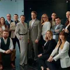 Grupa profesjonalistów w eleganckich strojach pozuje do zdjęcia w nowoczesnym wnętrzu.