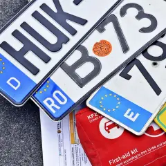 Kilka tablic rejestracyjnych z różnych krajów UE, dokumenty i apteczka. GKW rejestracja w tle.