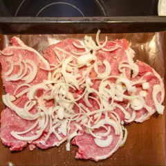 Plastry schabu pieczonego w cebulce, przyprawione i ułożone na blasze wyłożonej papierem do pieczenia.