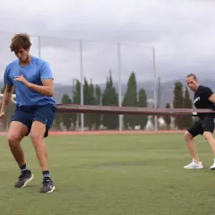 Zwei Männer trainieren auf einem Fußballfeld mit einem Widerstandsband für einen explosiven sprint.