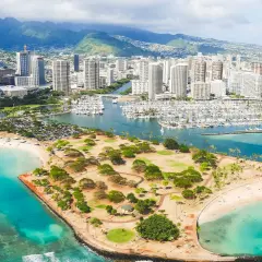 Widok na Honolulu, stolicę Hawajów, z plażą, parkiem i mariną pełną jachtów. W tle góry i drapacze chmur.