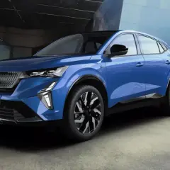 Une voiture hybride non rechargeable bleue, au design moderne, se gare devant un bâtiment aux lignes architecturales audacieuses.