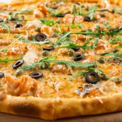 Pyszne ciasto na pizzę z krewetkami, oliwkami, kaparami i rukolą.