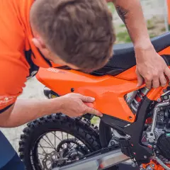 Mecánico ajusta panel en KTM 300 TPI. Se aprecia el motor y la rueda trasera.