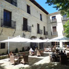 Disfruta de un día soleado donde comer en Santillana del Mar, con mesas al aire libre bajo sombrillas blancas, rodeado de arquitectura de piedra.
