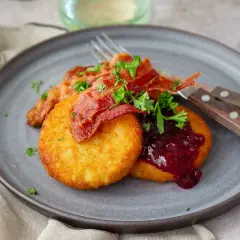 Gylla potatisbullar airfryer med knaprigt bacon, lingonsylt och persilja på en grå tallrik. En klassisk svensk rätt.