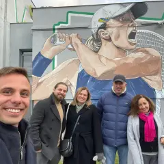 Grupa osób pozuje do zdjęcia na tle muralu Igi Świątek. To miejsce, gdzie mieszka Iga Świątek, jest pełne inspiracji.