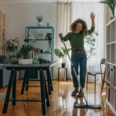 Donna sorridente lava il pavimento con uno straccio, un esempio di come tenere in ordine la casa con gioia.