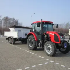 Czerwony traktor z przyczepą, gotowy do egzaminu na prawo jazdy na traktor. Litera "L" na zderzaku.