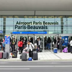 Voyageurs avec bagages devant l'aéroport Paris-Beauvais, prêts pour leur vol.