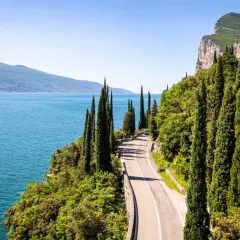 Route panoramique longeant un lac italien, idéale pour le camping-car. Cyprès élancés, falaises et eau bleue invitent à l'aventure.