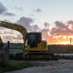 Żółta koparka Komatsu na tle zachodzącego słońca. Maszyna gotowa do pracy, nawet gdy dzień dobiega końca.