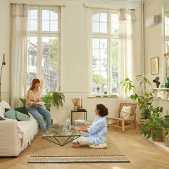 Dos mujeres disfrutan de un ambiente confortable en un salón luminoso, con el aire acondicionado en modo quiet funcionando discretamente.