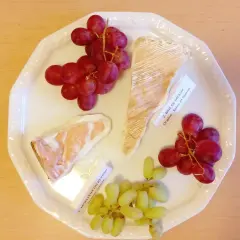 Talerz z serami Brie de Meaux i Moelleux du Revard, winogronami i etykietami, idealny do degustacji kuchni francuskiej.