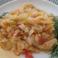 Młoda kapusta z pomidorami, duszona z koperkiem, na białym talerzu.