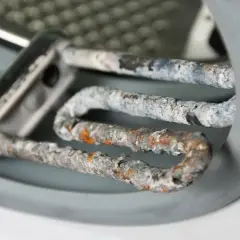 Stark verkalkter Heizstab einer Waschmaschine. Kalkablagerungen beeinträchtigen die Leistung und Lebensdauer. Zeit, die Waschmaschine zu entkalken!