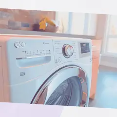 Un sèche-linge moderne dans une buanderie. Il est blanc avec une porte en verre chromé. Le panneau de commande est visible, avec un cadran et des boutons. On se demande combien de temps dure un sèche-linge pour un cycle complet.