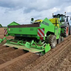 Zielona sadzarka ziemniaków z traktorem na polu. Maszyna wyznacza rzędy, pokazując, na jaką głębokość sadzić ziemniaki.