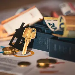 Llave dorada sobre silueta de casa, billetes y monedas. Representa el alquiler con opción a compra entre particulares.