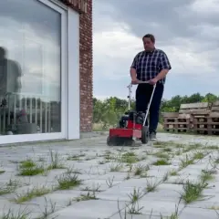 Mężczyzna używa maszyny do czyszczenia kostki brukowej, pokazując, jak usunąć mech z kostki.