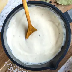 Cremige Bechamel-Sauce in einer Pfanne, bereit für die Lasagne. Butter, Milch und Gewürze sind daneben zu sehen.