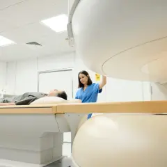 Pacjent leży na łóżku podczas badania rezonans magnetyczny barku. Technik przygotowuje aparat.