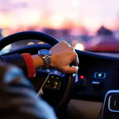 Förare med klocka styr bil med automatlåda genom stadens ljus i skymningen.