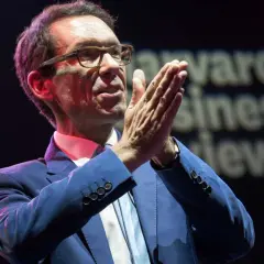 Byron Sharp, w okularach i niebieskim garniturze, z dłońmi złożonymi w geście przemowy, na tle napisu "Harvard Business Review".