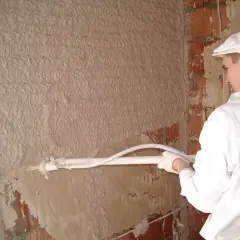 Pracownik nakłada tynk maszynowy na ścianę. Czy tynki maszynowe trzeba szpachlować? Zależy od efektu końcowego.