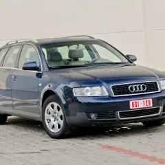 Ciemnoniebieskie Audi A4 B6 Avant na parkingu. Widać przednie reflektory i grill z logo Audi.