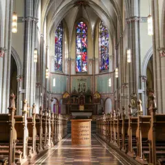 Blick in den katholischen Kircheninnenraum mit Holzbänken, Buntglasfenstern und einem Altar.