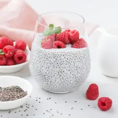 Pyszny deser chia pudding z malinami i miętą, obok miseczka z nasionami chia i świeżymi malinami.