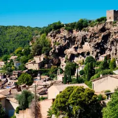 Vue d'un village perché du Var, accroché à une falaise rocheuse, avec des maisons aux toits de tuiles et une tour médiévale.